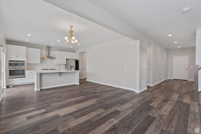 kitchen featuring open floor plan, light countertops, a notable chandelier, appliances with stainless steel finishes, and wall chimney exhaust hood