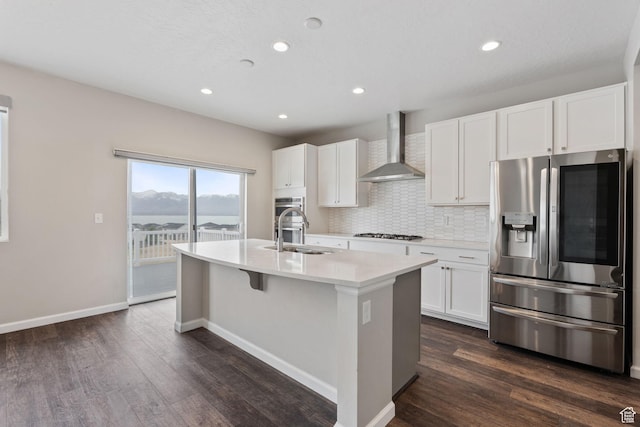 kitchen featuring dark wood-style flooring, stainless steel appliances, backsplash, a center island with sink, and wall chimney range hood