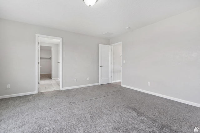 unfurnished bedroom featuring light carpet, baseboards, and a walk in closet