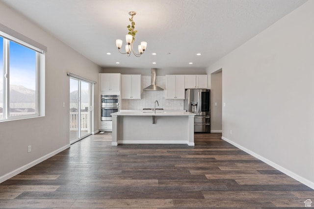 kitchen with a notable chandelier, a sink, wall chimney exhaust hood, tasteful backsplash, and stainless steel appliances