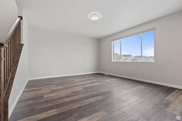 spare room with baseboards, a textured ceiling, and dark wood finished floors