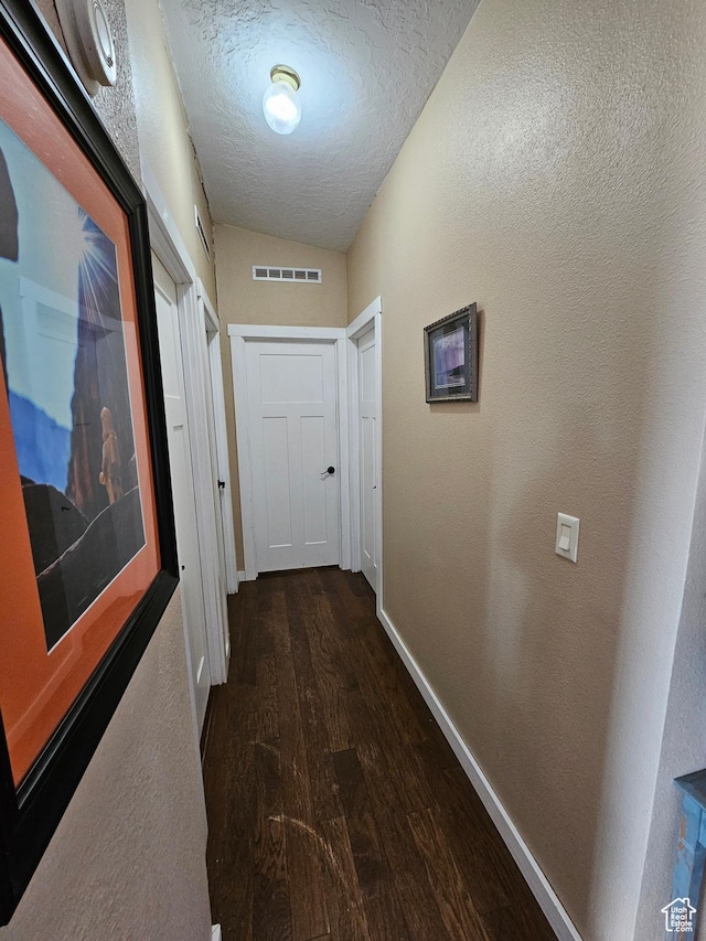 corridor with a textured ceiling, visible vents, baseboards, dark wood-style floors, and a textured wall