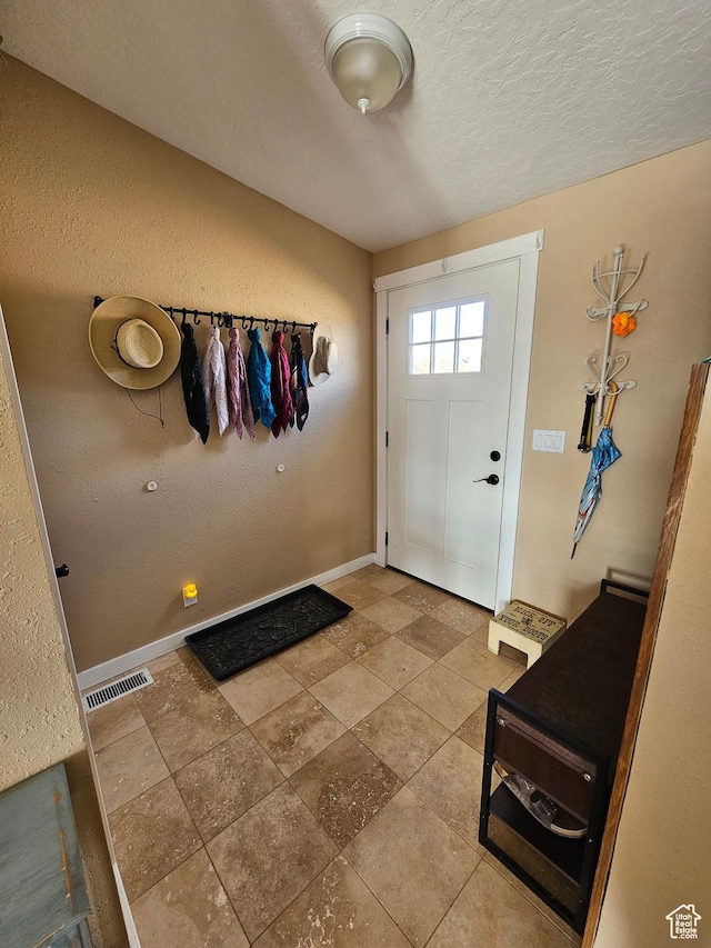 doorway featuring baseboards, a textured ceiling, visible vents, and a textured wall