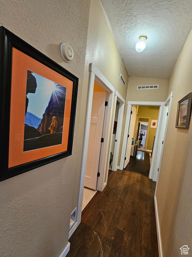 hallway featuring baseboards, a textured ceiling, visible vents, and wood finished floors