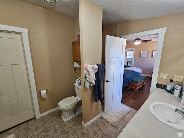 bathroom with toilet, vanity, a ceiling fan, a textured ceiling, and baseboards