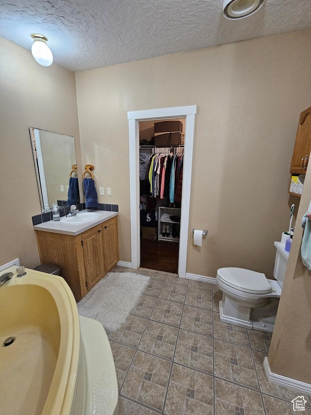 bathroom with a textured ceiling, baseboards, toilet, vanity, and a spacious closet