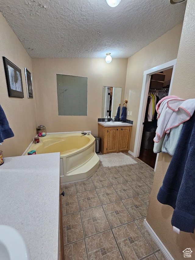 full bathroom featuring a textured ceiling, baseboards, vanity, a garden tub, and a walk in closet