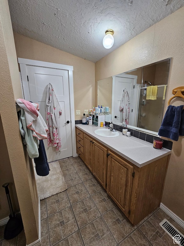 full bathroom featuring vanity, baseboards, a shower stall, a textured ceiling, and visible vents