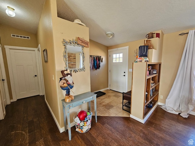 foyer entrance with lofted ceiling, visible vents, wood finished floors, and a textured ceiling