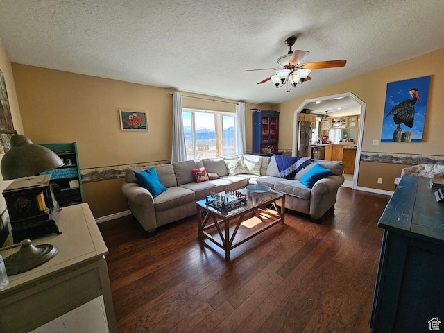 living room featuring a textured ceiling, baseboards, ceiling fan, dark wood finished floors, and arched walkways