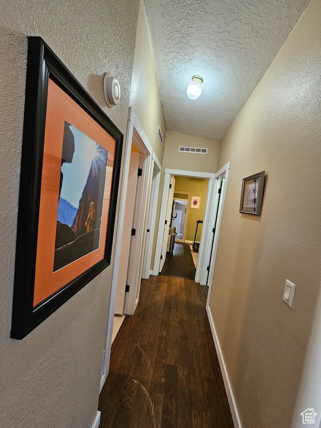 corridor with a textured ceiling, visible vents, baseboards, wood finished floors, and a textured wall