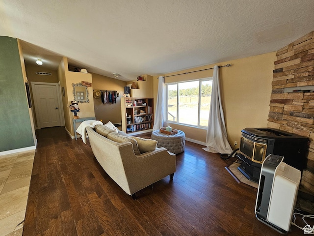 living area with a textured ceiling, visible vents, baseboards, wood finished floors, and a wood stove