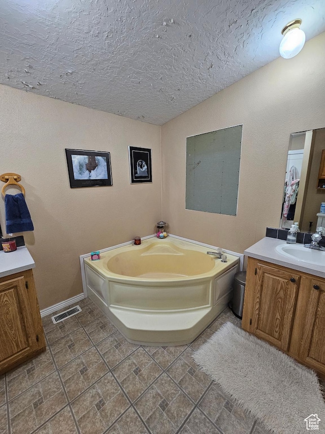 bathroom with vanity, baseboards, a textured ceiling, a garden tub, and visible vents
