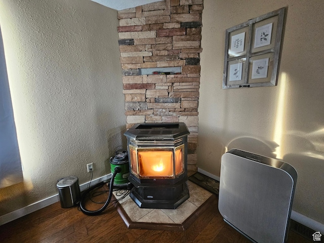room details featuring wood finished floors, a textured wall, baseboards, and a wood stove