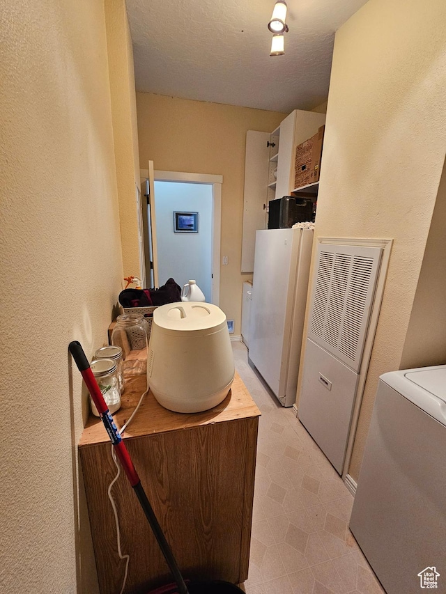 interior space featuring a textured wall, a heating unit, washer / dryer, laundry area, and light floors