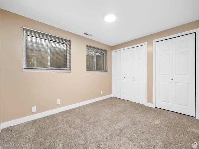 unfurnished bedroom featuring baseboards, visible vents, two closets, and carpet