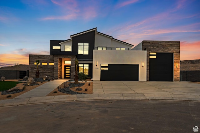 contemporary house featuring stone siding, a balcony, driveway, an attached garage, and stucco siding