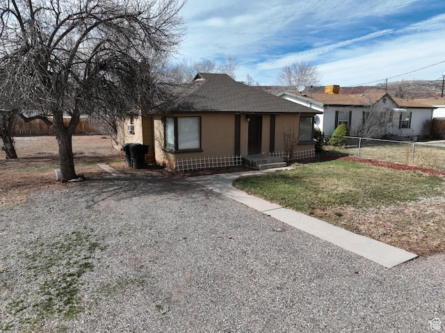 view of front of home featuring stucco siding, fence, gravel driveway, a front lawn, and a shingled roof