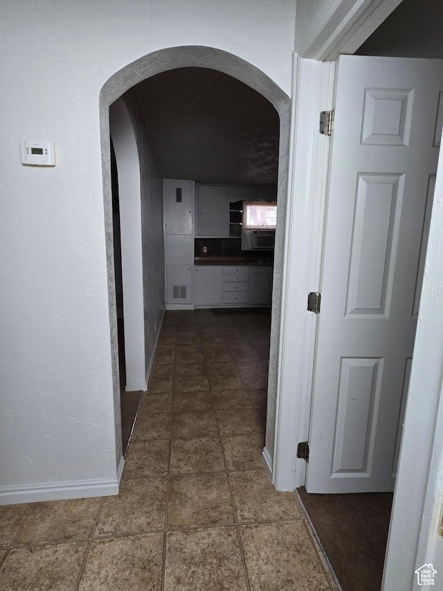 hallway featuring arched walkways, baseboards, visible vents, and tile patterned flooring