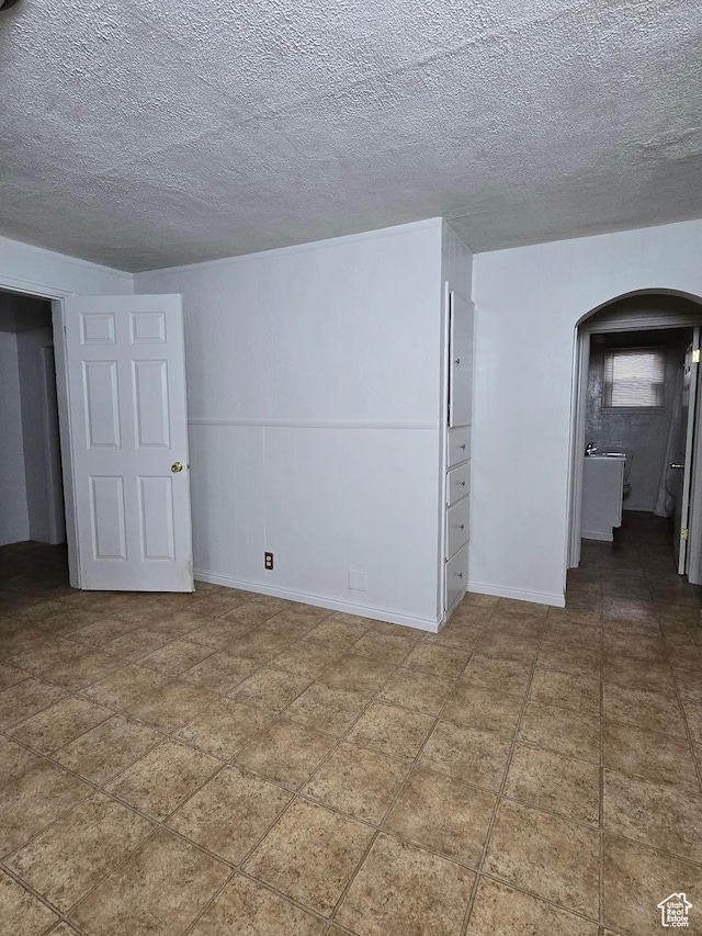empty room with arched walkways, baseboards, and a textured ceiling