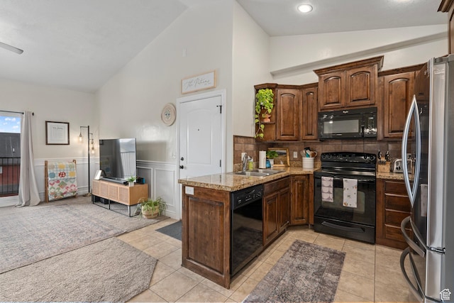 kitchen featuring a wainscoted wall, a sink, light stone countertops, light tile patterned floors, and black appliances