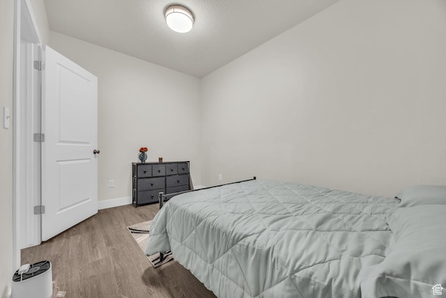 bedroom featuring a textured ceiling, baseboards, and wood finished floors