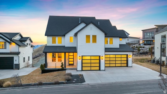 view of front of property featuring an attached garage, concrete driveway, covered porch, and roof with shingles