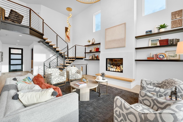 living area with stairs, a towering ceiling, wood finished floors, and a glass covered fireplace