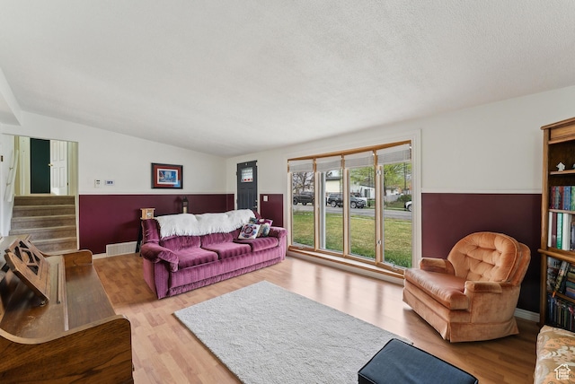 living room featuring stairs, vaulted ceiling, wood finished floors, and a textured ceiling