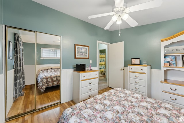bedroom with a closet, a wainscoted wall, ceiling fan, and wood finished floors