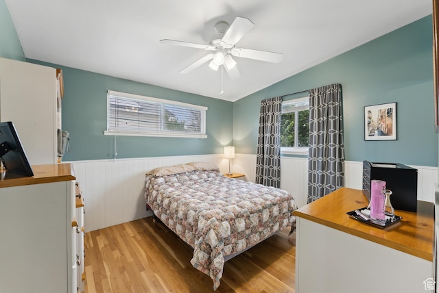bedroom with a wainscoted wall, light wood-type flooring, ceiling fan, and vaulted ceiling