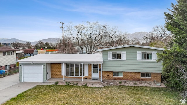 tri-level home featuring covered porch, concrete driveway, an attached garage, a front lawn, and a mountain view