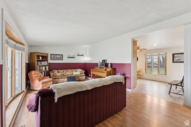 living room with lofted ceiling, light wood-style flooring, ceiling fan, and a textured ceiling