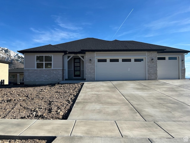 prairie-style house with driveway, a garage, and stone siding