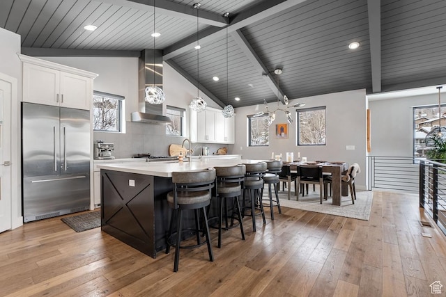 8680 Saddleback Cir, Park City, UT 84098 - kitchen featuring built in fridge, wall chimney exhaust hood, a center island with sink, light countertops, and light wood-style floors
