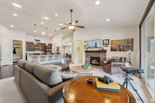 living area featuring high vaulted ceiling, light wood finished floors, ceiling fan, recessed lighting, and a stone fireplace