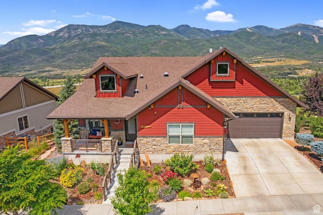 view of front of house with a mountain view, driveway, stone siding, a porch, and a garage