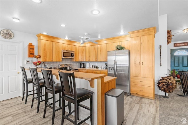 170 E 400 N, Mount Pleasant, UT 84647 - kitchen with decorative backsplash, a peninsula, stainless steel appliances, a ceiling fan, and a breakfast bar area