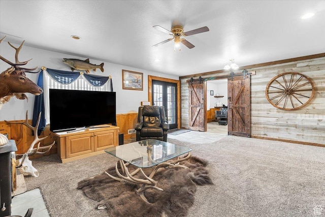 170 E 400 N, Mount Pleasant, UT 84647 - living room featuring wood walls, light colored carpet, a barn door, a ceiling fan, and wainscoting