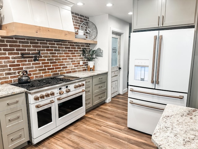 690 N Main St, Antimony, UT 84712 - kitchen featuring light stone counters, light wood-style floors, premium range hood, and white appliances