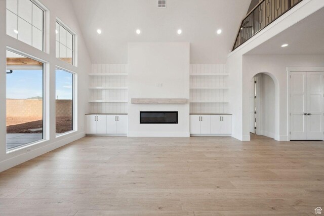 3087 E 2220 S, St George, UT 84790 - unfurnished living room with high vaulted ceiling, arched walkways, light wood-style floors, a glass covered fireplace, and built in shelves