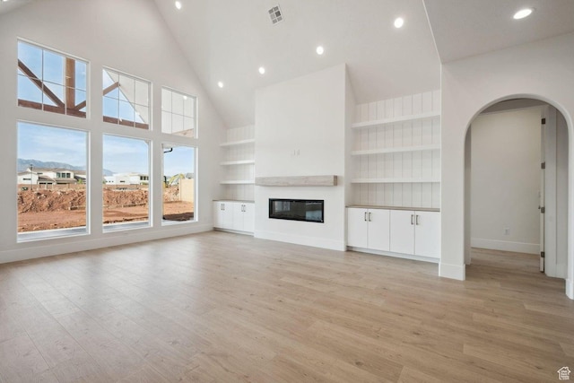 3087 E 2220 S, St George, UT 84790 - unfurnished living room featuring high vaulted ceiling, baseboards, light wood-type flooring, a glass covered fireplace, and arched walkways
