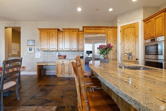 kitchen featuring a kitchen breakfast bar, stainless steel appliances, a sink, light stone counters, and backsplash