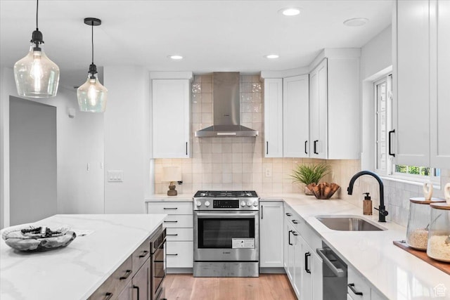 kitchen with light stone countertops, a sink, wall chimney range hood, white cabinets, and appliances with stainless steel finishes