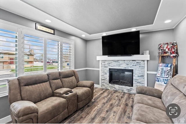 living room featuring recessed lighting, a stone fireplace, baseboards, and wood finished floors