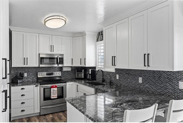 kitchen featuring white cabinetry, a peninsula, dark stone countertops, stainless steel appliances, and decorative backsplash