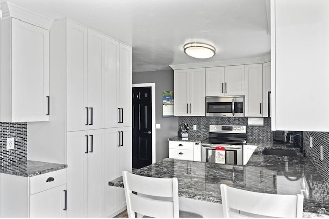 kitchen featuring white cabinetry, a sink, stainless steel appliances, and dark stone counters