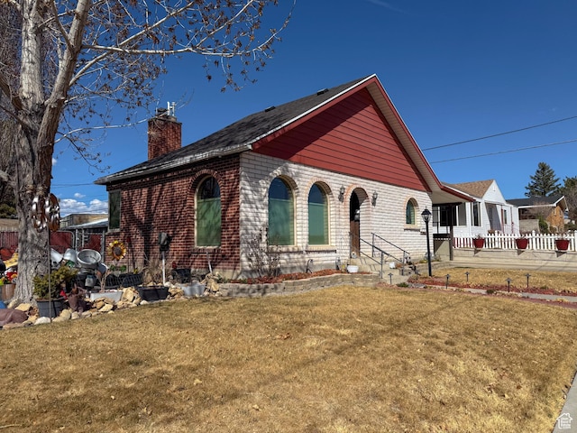 view of front of house featuring a front lawn, a chimney, fence, and brick siding