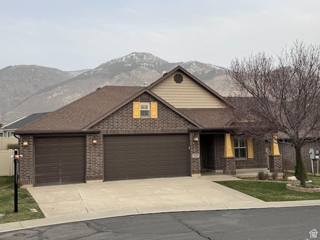 view of front of house with concrete driveway, roof with shingles, an attached garage, brick siding, and a mountain view