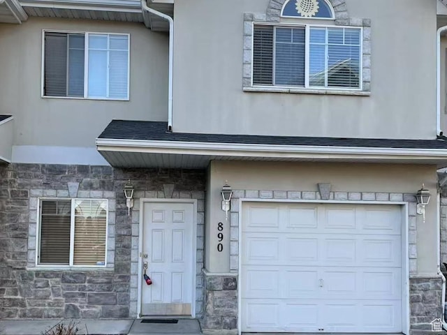 entrance to property with stucco siding, an attached garage, and stone siding
